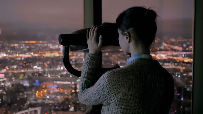 年轻女子透过旅游望远镜探索城市夜景