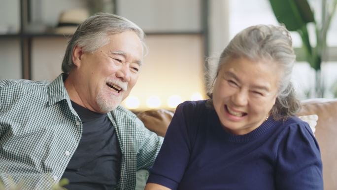 亚洲老年退休夫妇在沙发上谈笑风生