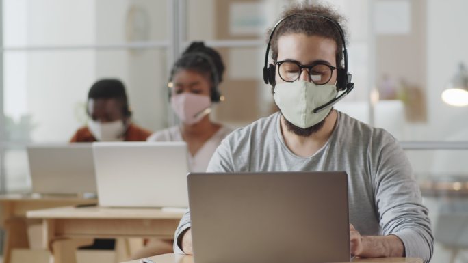 戴着口罩在办公室笔记本电脑上工作的男性