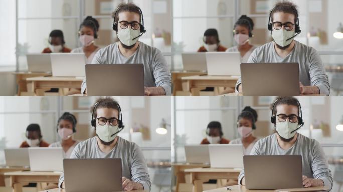 戴着口罩在办公室笔记本电脑上工作的男性