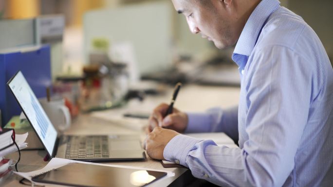 男性商务人士办公室使用笔记本电脑和笔工作