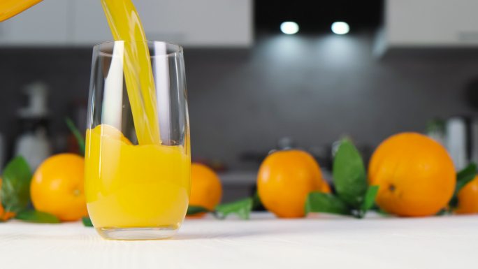 橙汁倒进白桌子上的玻璃杯里