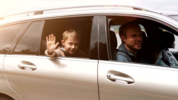一家人开车离开：男孩从开着的窗户挥手