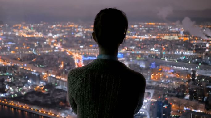 沉思的女人从摩天大楼上看城市夜景