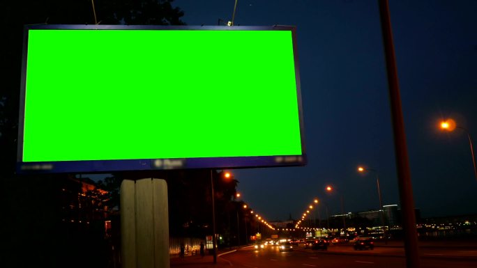 繁忙的夜间街道上的绿色屏幕广告牌