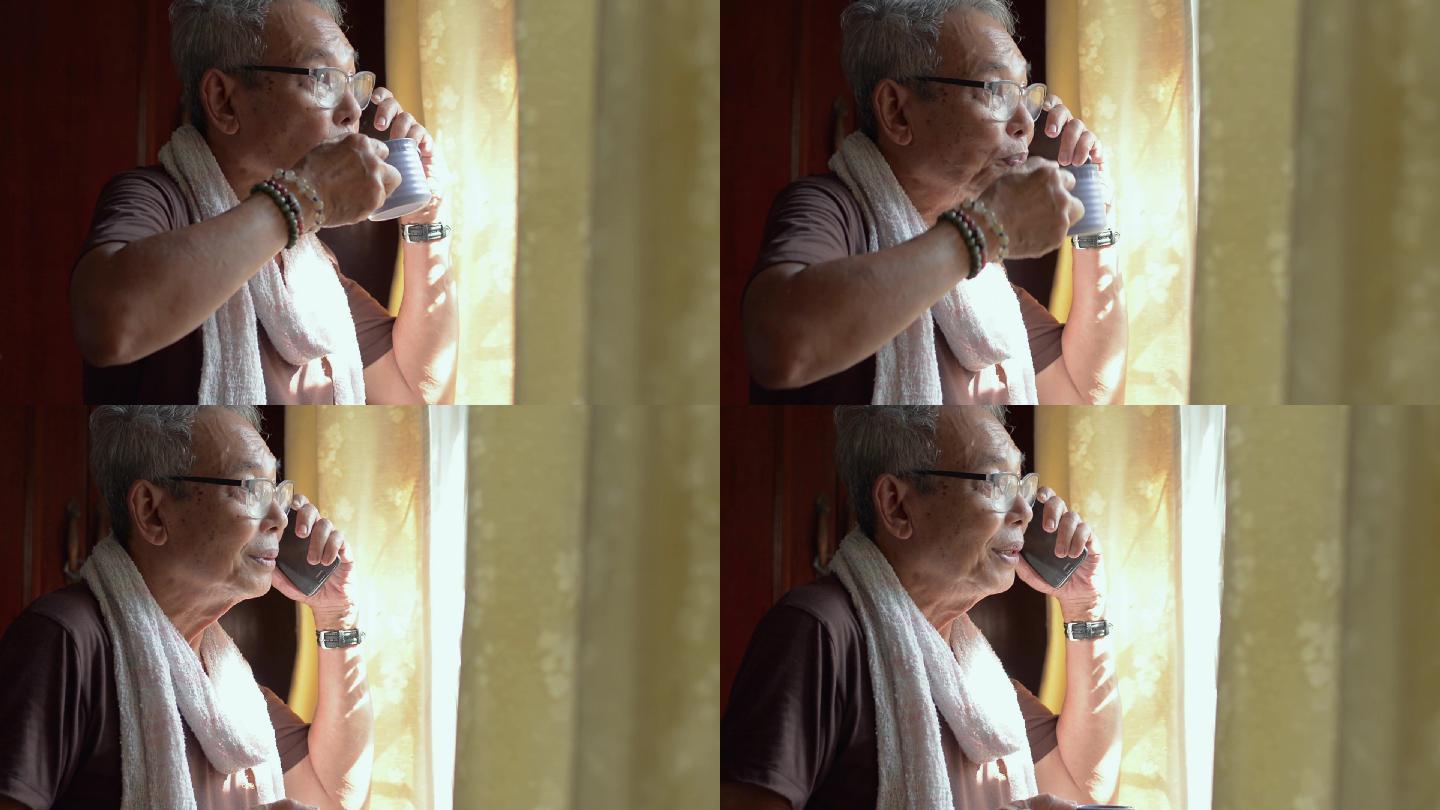 老人戴着眼镜一边打电话，一边喝热咖啡