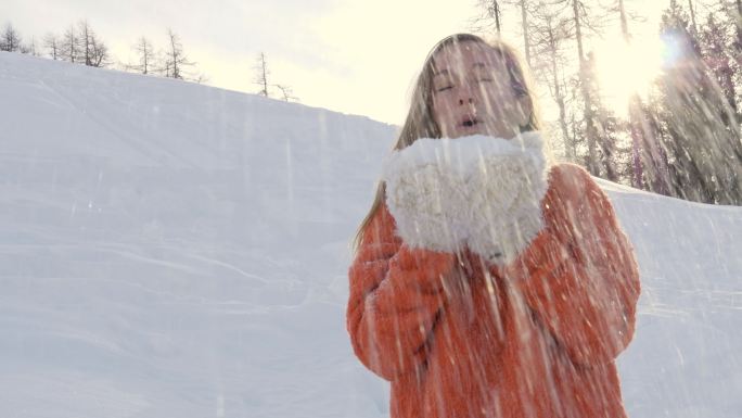 一名年轻女子站在雪地里用手吹雪。