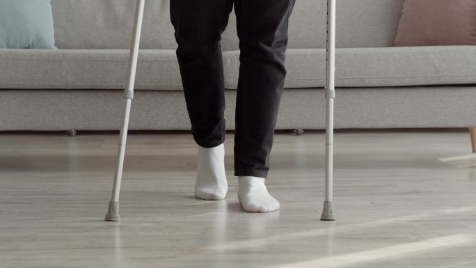 跛脚男子拄着拐杖在家走路