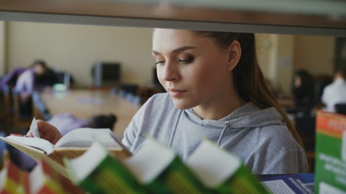 女学生站在书架旁，手里拿着一本书