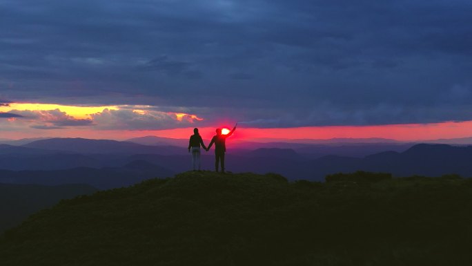 这对夫妇拿着烟火棒站在日落背景下的山上
