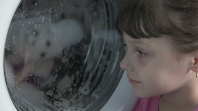 一个小女孩看着房间里正在工作的洗衣机