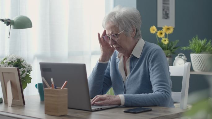 疲惫的老妇人正在使用笔记本电脑，头痛不已