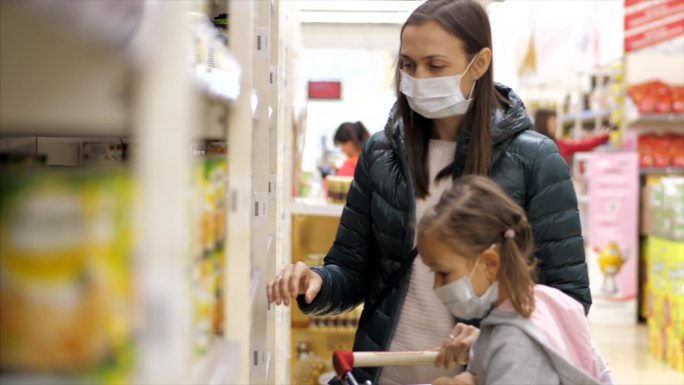 一名戴着医用口罩的小女孩在超市买罐头食品
