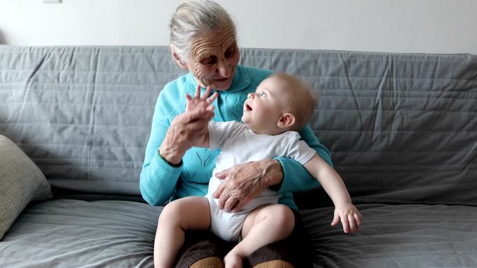 一位老奶奶坐在沙发上，怀里抱着一个小孙子