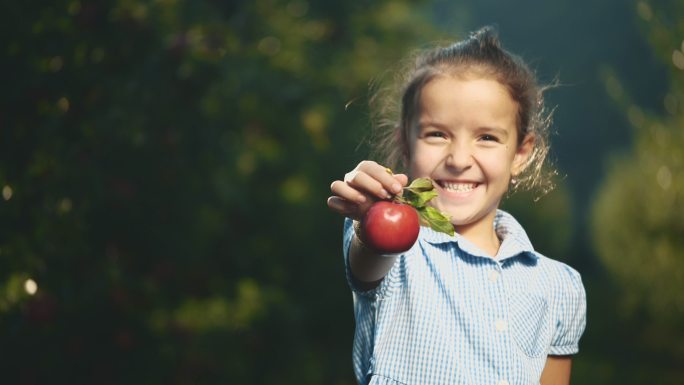 小女孩在户外献上一个红苹果