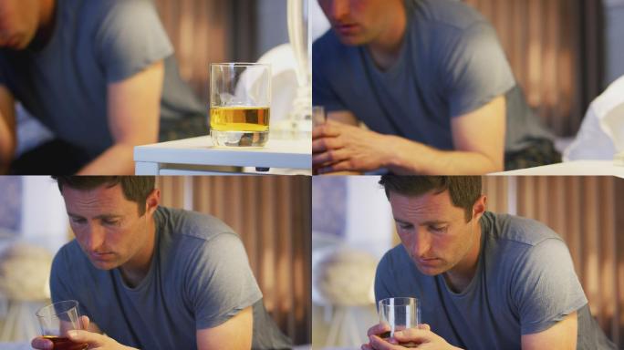抑郁的男人穿着睡衣坐在床边喝一杯威士忌