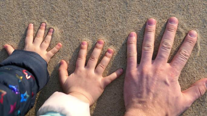 日落时，成人和儿童的手在沙滩上留下手印