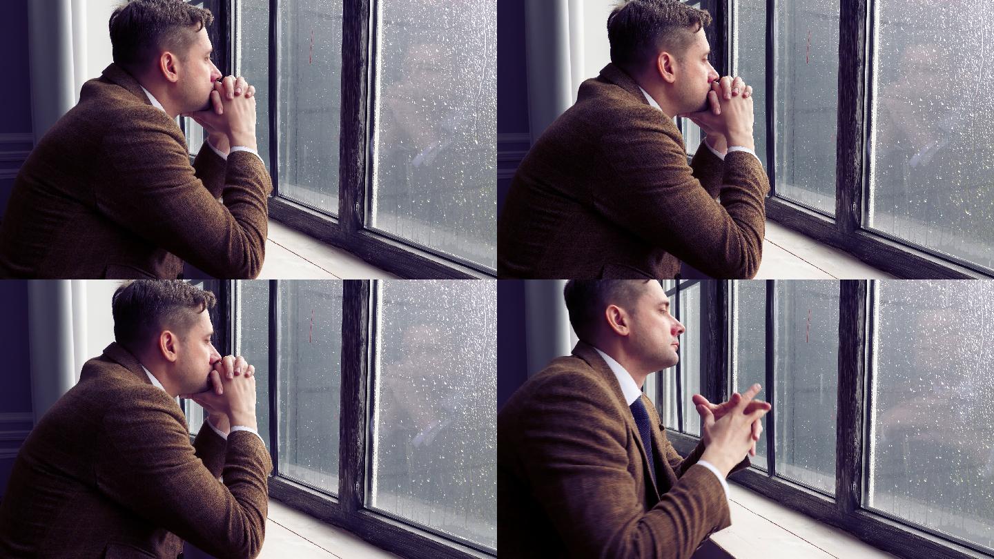 一个穿着西装的忧郁男人站在窗前
