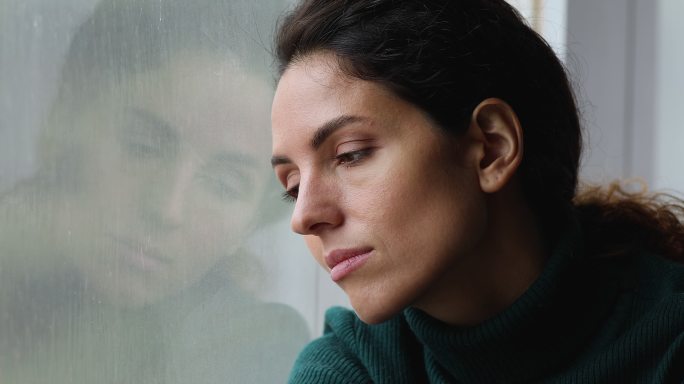 悲伤的女人坐在窗台上看着外面的雨天