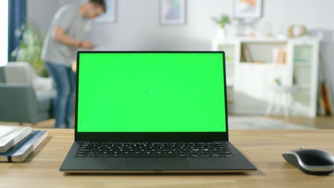 桌上放着一台带有绿色屏幕的笔记本电脑