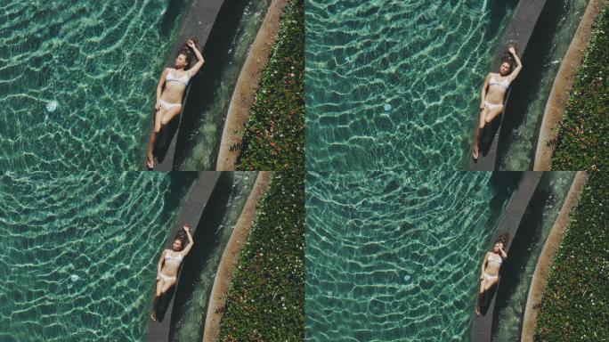 身穿白色比基尼的美女躺在度假泳池旁晒太阳
