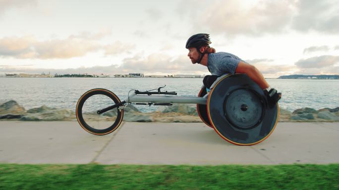 残障轮椅运动员在日落时推着赛车椅锻炼身体