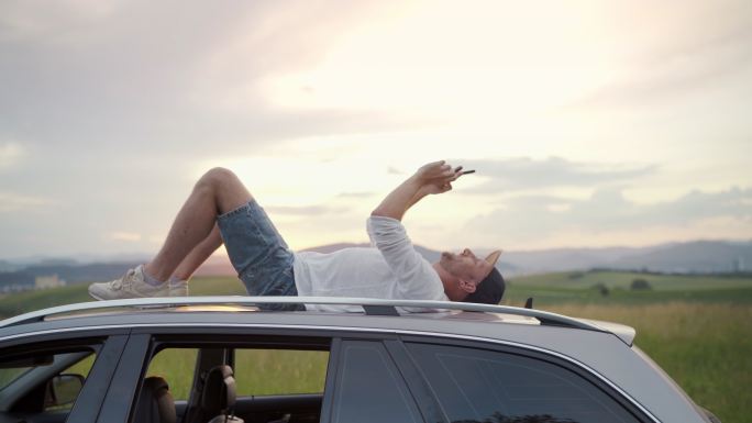一个年轻人躺在车顶上通过电话聊天