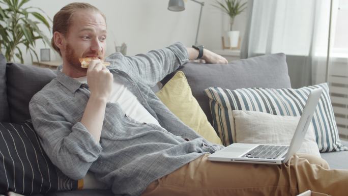 男人在笔记本电脑上看电影吃披萨