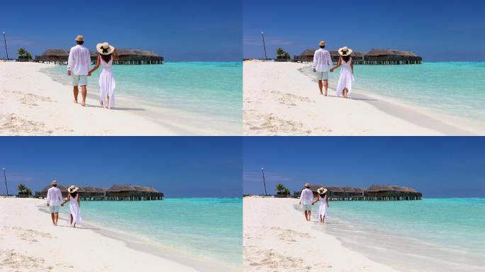一对穿着白色衣服的幸福夫妇沿着热带海滩散步