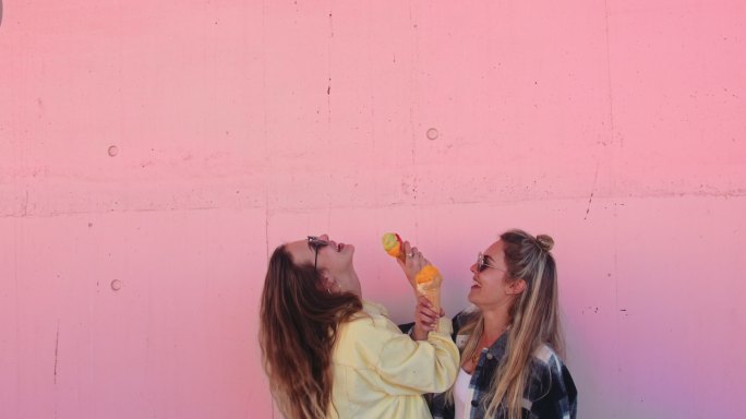 女人在粉红色的墙上舔冰淇淋