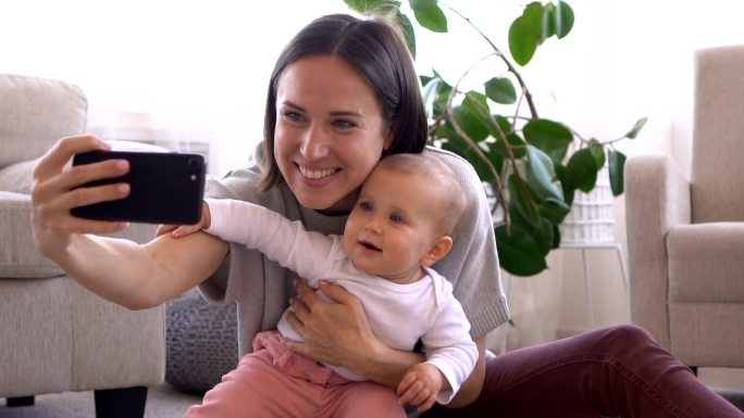 快乐的妈妈在家里用手机摄像头和女婴自拍
