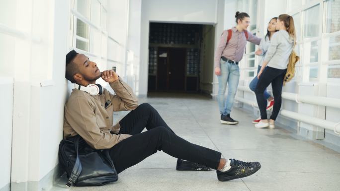 严肃非裔男学生坐在大学走廊的地板上