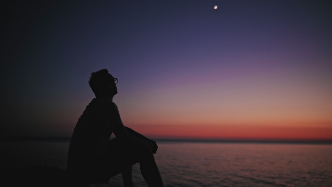 一个男人在海平线上看月亮和星星的剪影