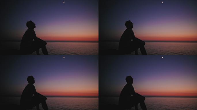 一个男人在海平线上看月亮和星星的剪影