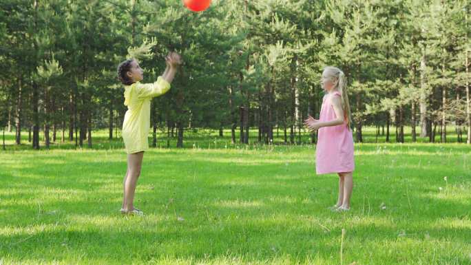 两个小女孩站在公园的绿色草坪上玩红球