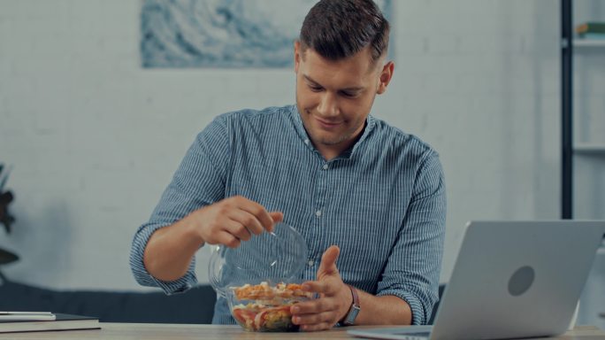 英俊的自由职业者使用笔记本电脑吃沙拉