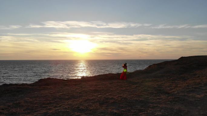 身穿红色长裙的美女在山岩上眺望大海