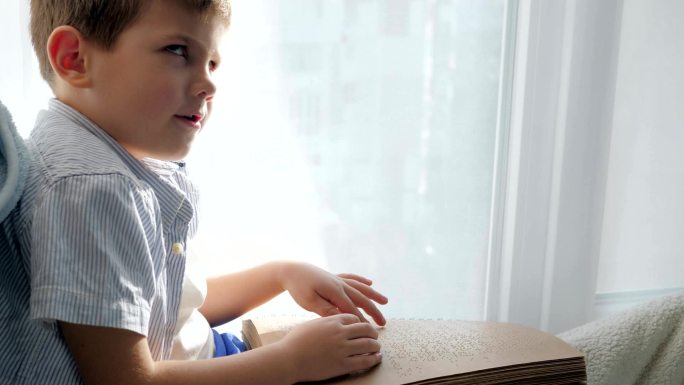 抱着盲文书坐在窗台上看字的儿童