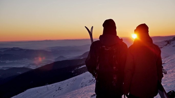 滑雪的情侣一起在山顶欣赏日落
