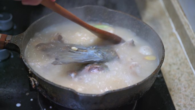 一位厨师在煮鱼头汤，煎鱼头并加水熬汤