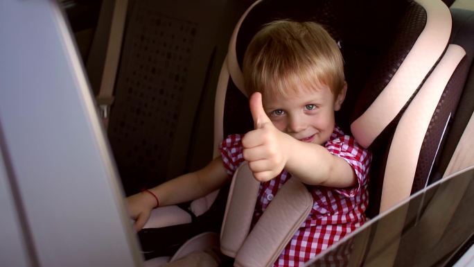 小男孩坐在儿童座椅上竖起大拇指。