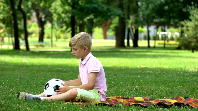 悲伤的男孩坐在公园里扔球