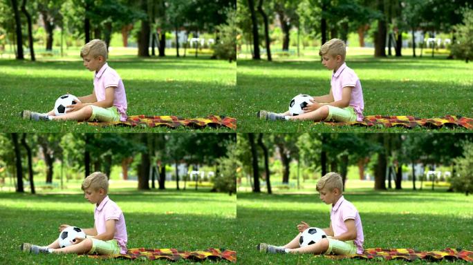 悲伤的男孩坐在公园里扔球