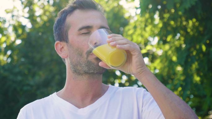 男人在户外喝着一杯富含维生素的橙汁