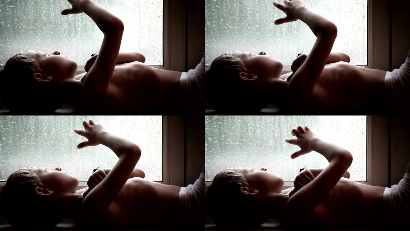 窗台上的男孩看着玻璃上的雨滴