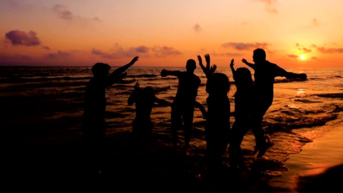 日落时四个朋友在海边跳舞的剪影