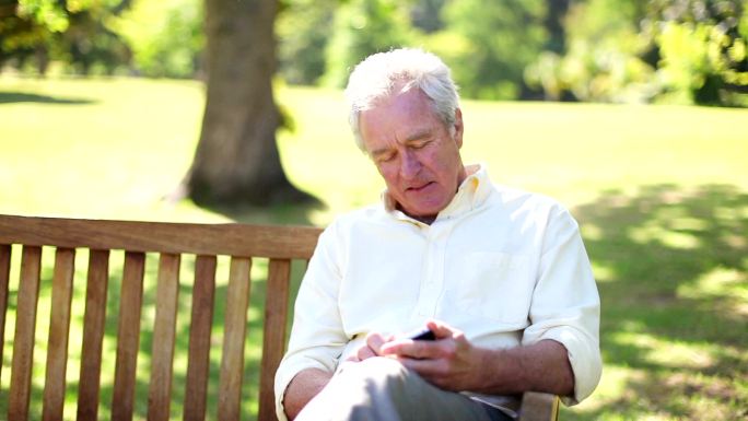 坐在长凳上使用手机的退休男子