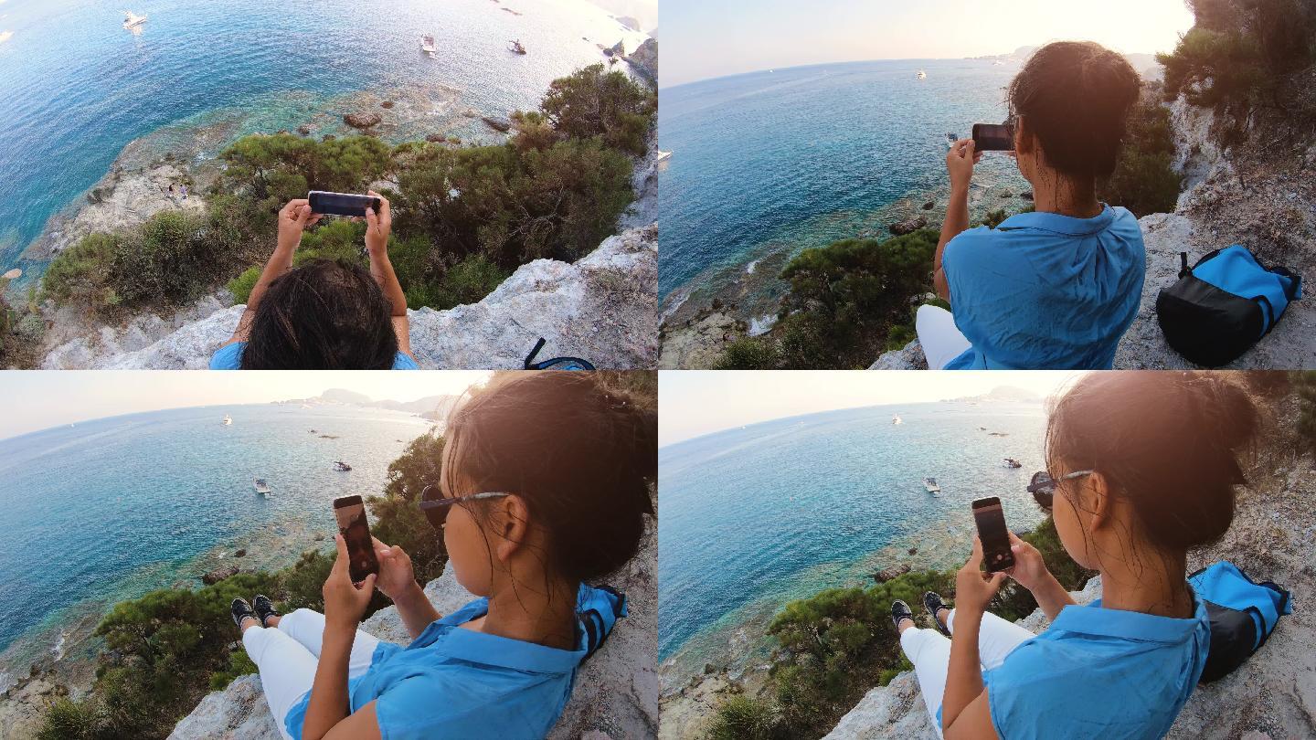 年轻女子坐在悬崖边用手机拍照