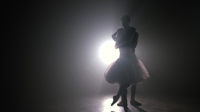 一对芭蕾舞演员在黑暗的舞台上练习动作。