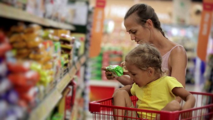 母亲和小女儿在超市的糖果区挑选零食